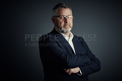 Buy stock photo Studio portrait of a handsome mature businessman standing with his arms folded against a dark background