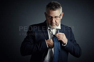 Buy stock photo Studio shot of a handsome mature businessman fastening his tie while standing against a dark background