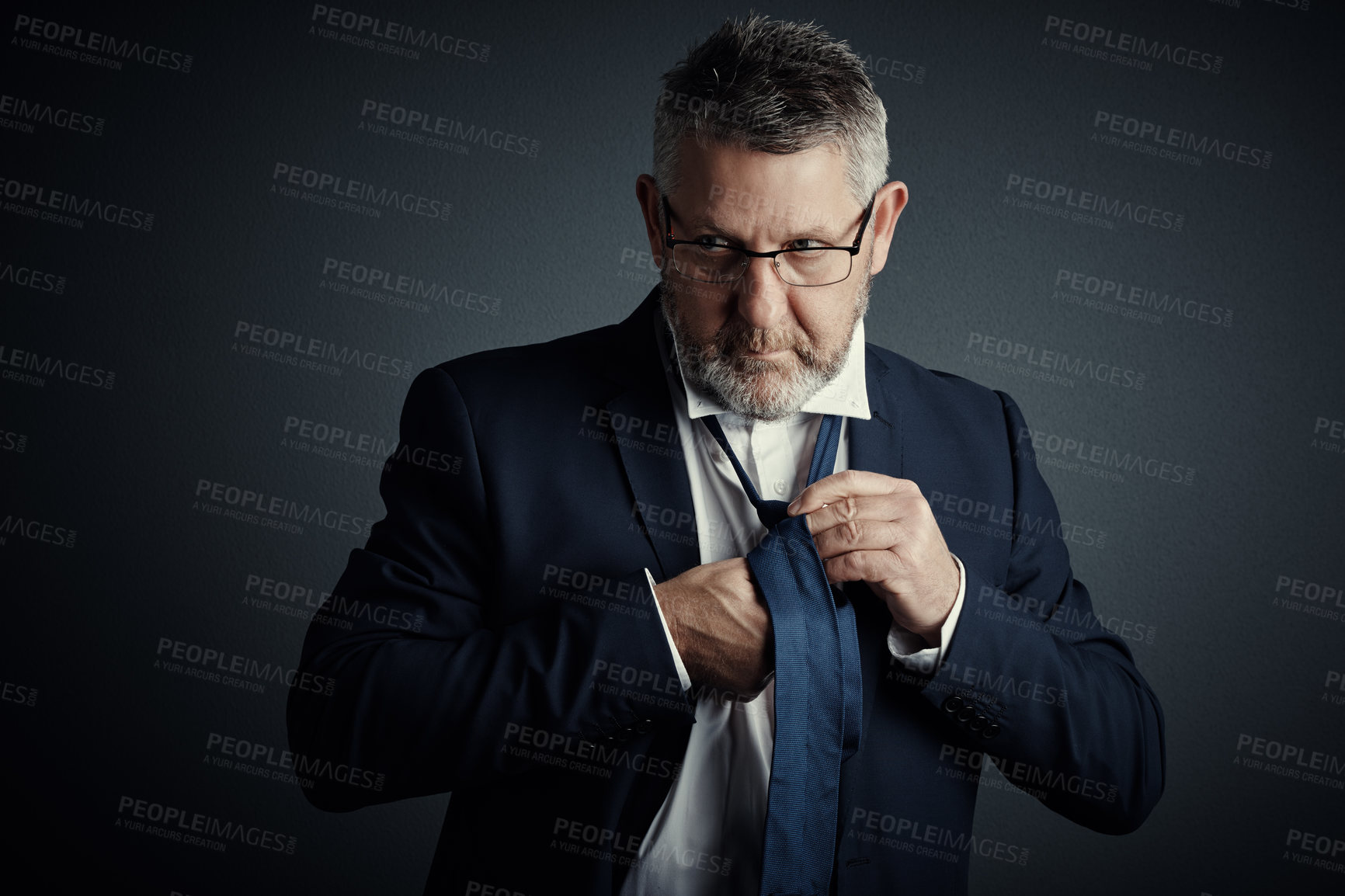 Buy stock photo Studio shot of a handsome mature businessman fastening his tie while standing against a dark background