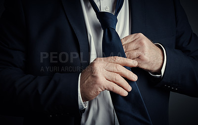 Buy stock photo Studio shot of an unrecognizable mature businessman fastening his tie while standing against a dark background