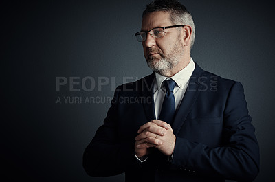 Buy stock photo Studio shot of a handsome mature businessman looking thoughtful while standing against a dark background