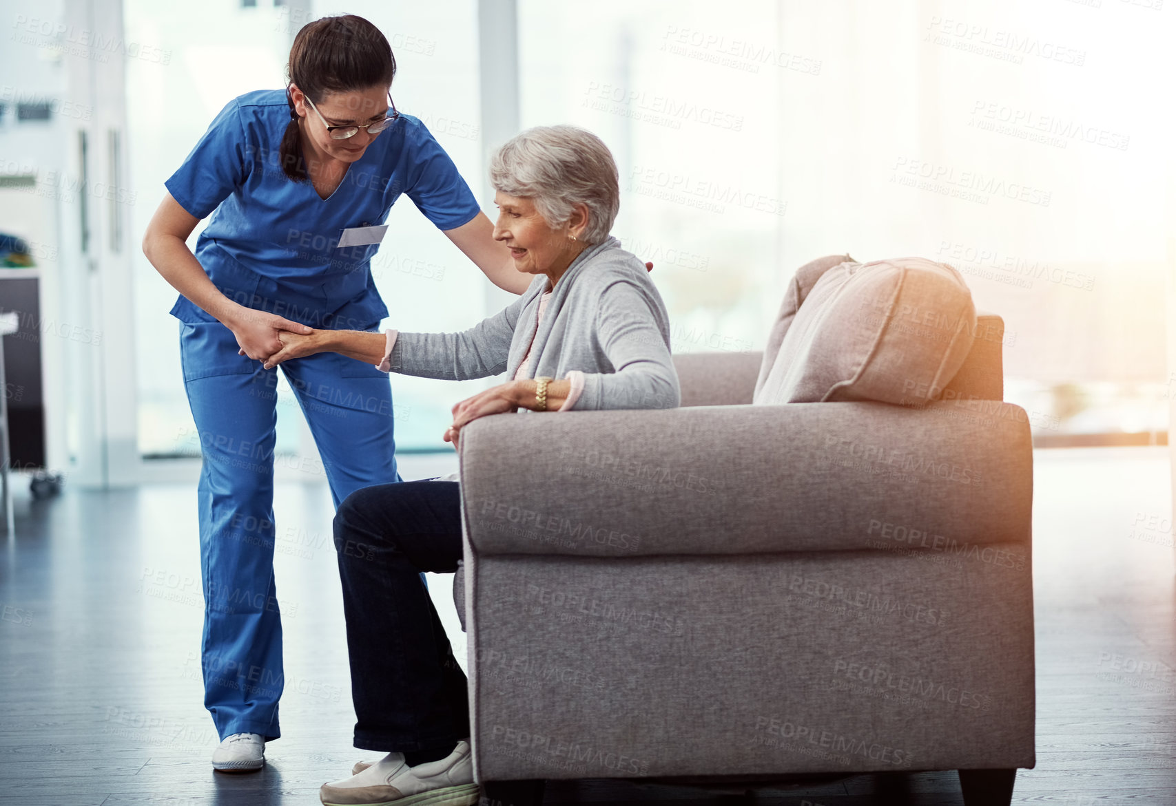 Buy stock photo Full length shot of a young female nurse helping her senior patient up from a chair in the old age home