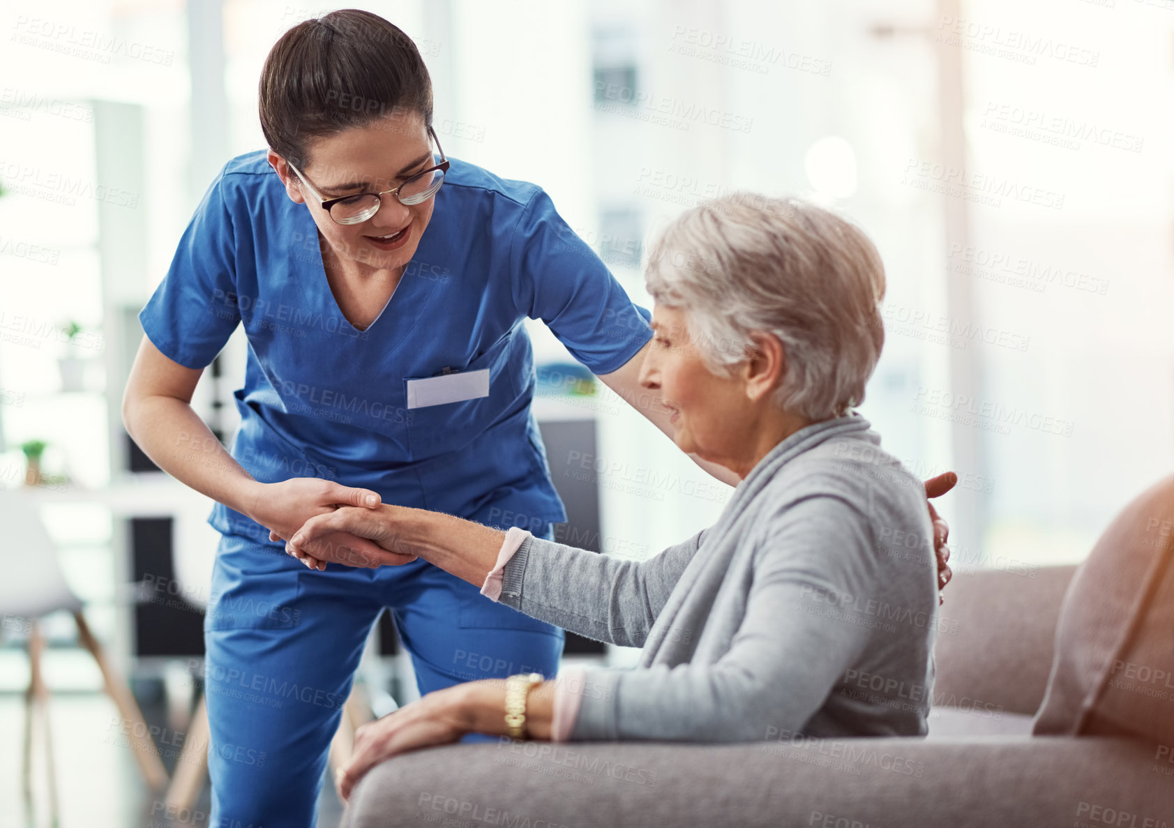 Buy stock photo Cropped shot of a young female nurse helping her senior patient up from a chair in the old age home