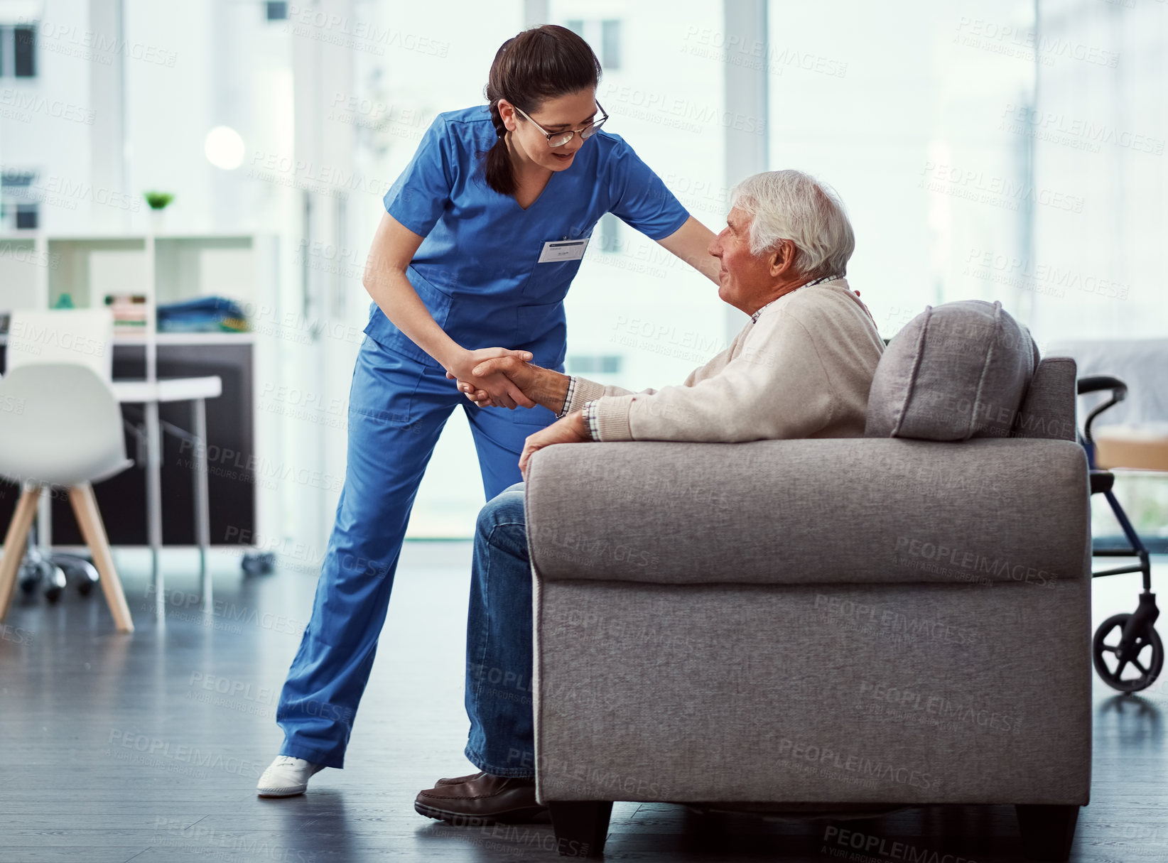 Buy stock photo Full length shot of a young female nurse helping her senior patient up from a chair in the old age home