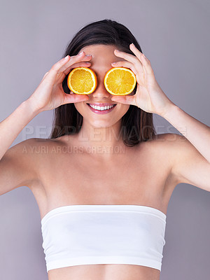 Buy stock photo Studio shot of an attractive young woman holding oranges in front of her eyes against a purple background