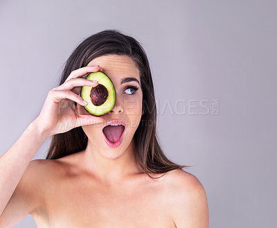 Buy stock photo Studio shot of an attractive young woman covering her eye with an avocado against a purple background