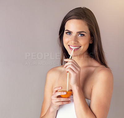 Buy stock photo Studio portrait of an attractive young woman drinking from an orange against a purple background