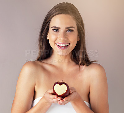 Buy stock photo Studio portrait of an attractive young woman holding an apple against a brown background