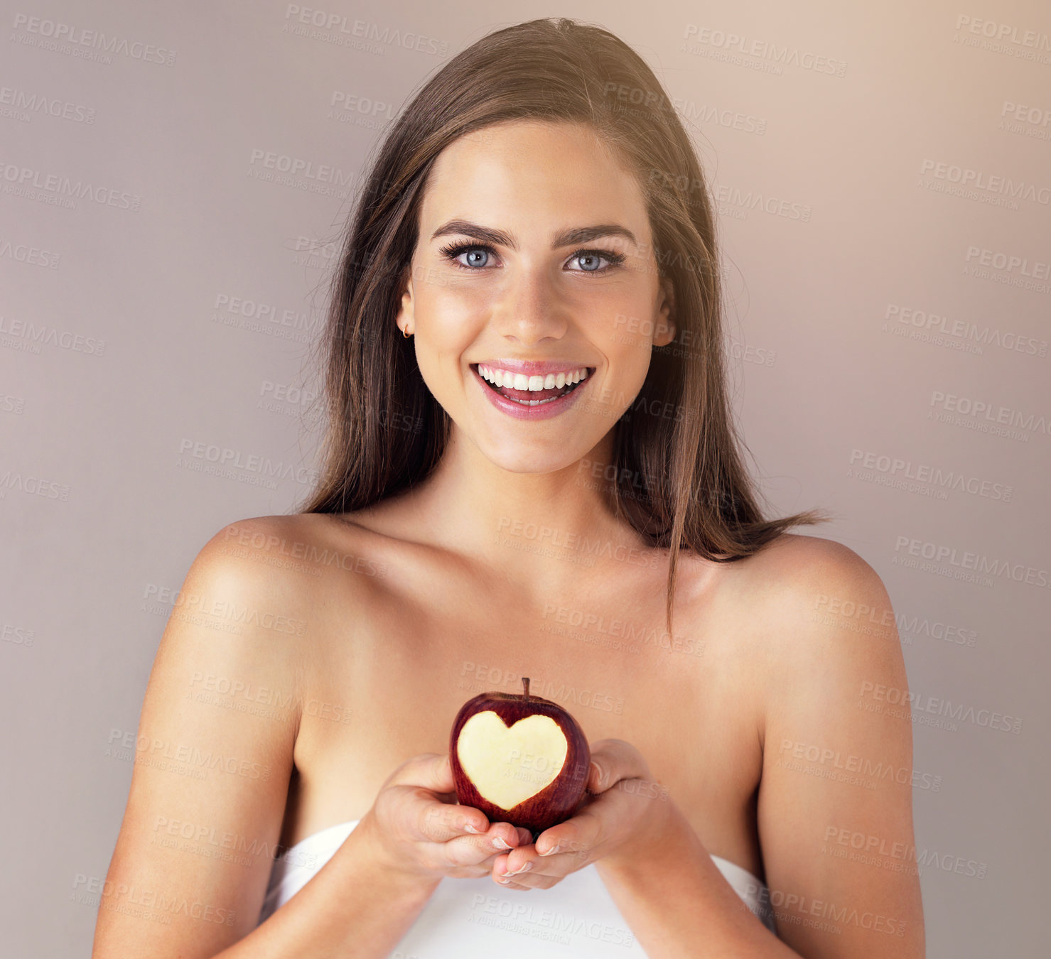 Buy stock photo Heart, apple and portrait of woman in studio for health, wellness and diet snack for nutrition. Smile, vitamins and female person with bite in organic, fresh or natural fruit by gray background.