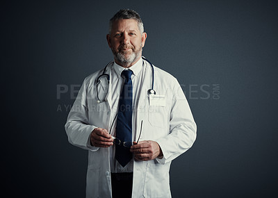 Buy stock photo Studio portrait of a handsome mature male doctor standing against a dark background