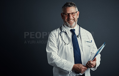 Buy stock photo Studio portrait of a handsome mature male doctor holding medical records while standing against a dark background