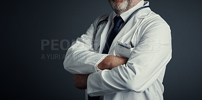 Buy stock photo Studio shot of an unrecognizable male doctor standing with his arms folded against a dark background