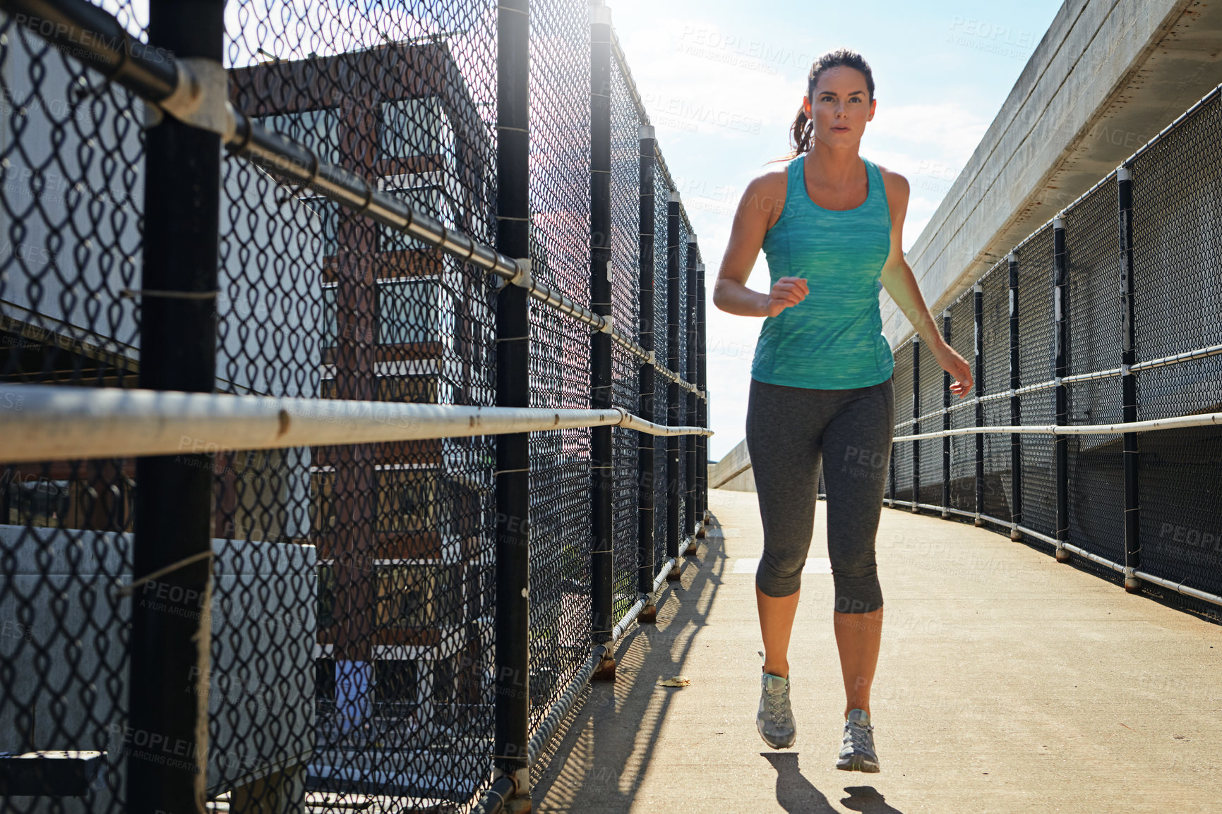 Buy stock photo Shot of a sporty young woman running on a footbridge