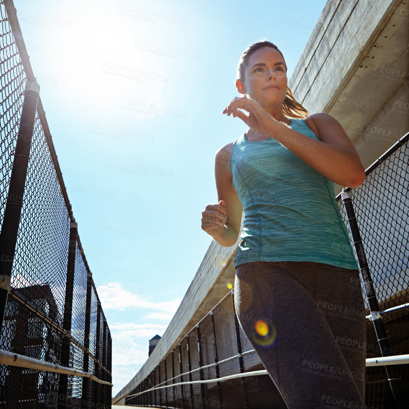 Buy stock photo Shot of a sporty young woman running on a footbridge