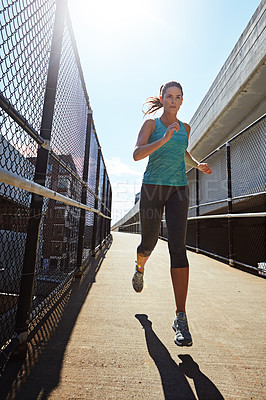 Buy stock photo Shot of a sporty young woman running on a footbridge