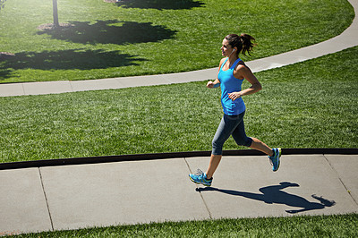 Buy stock photo Shot of a young woman listening to music while out running