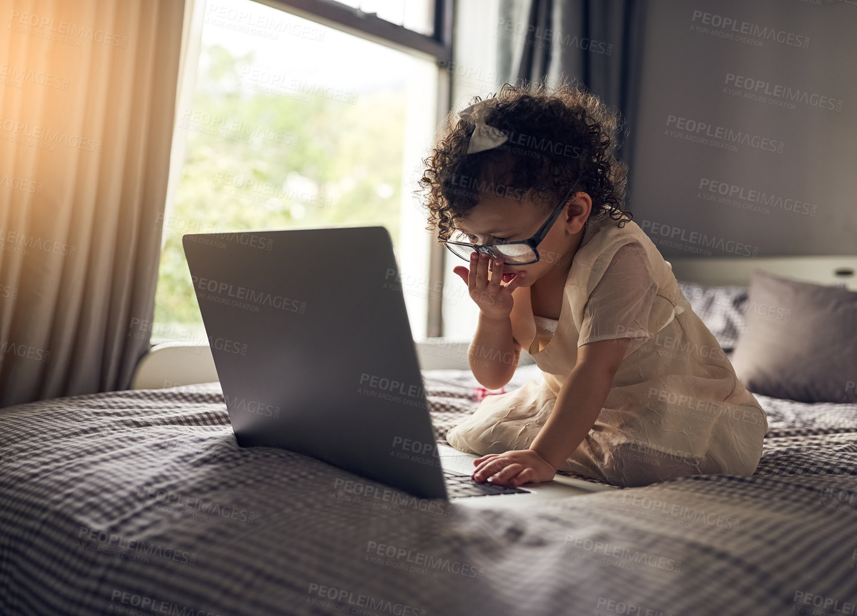 Buy stock photo Full length shot of an adorable little girl using a laptop while sitting on a bed