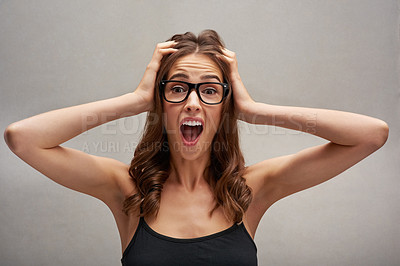 Buy stock photo Studio portrait of an attractive young woman looking shocked with her hands in her hair against a grey background
