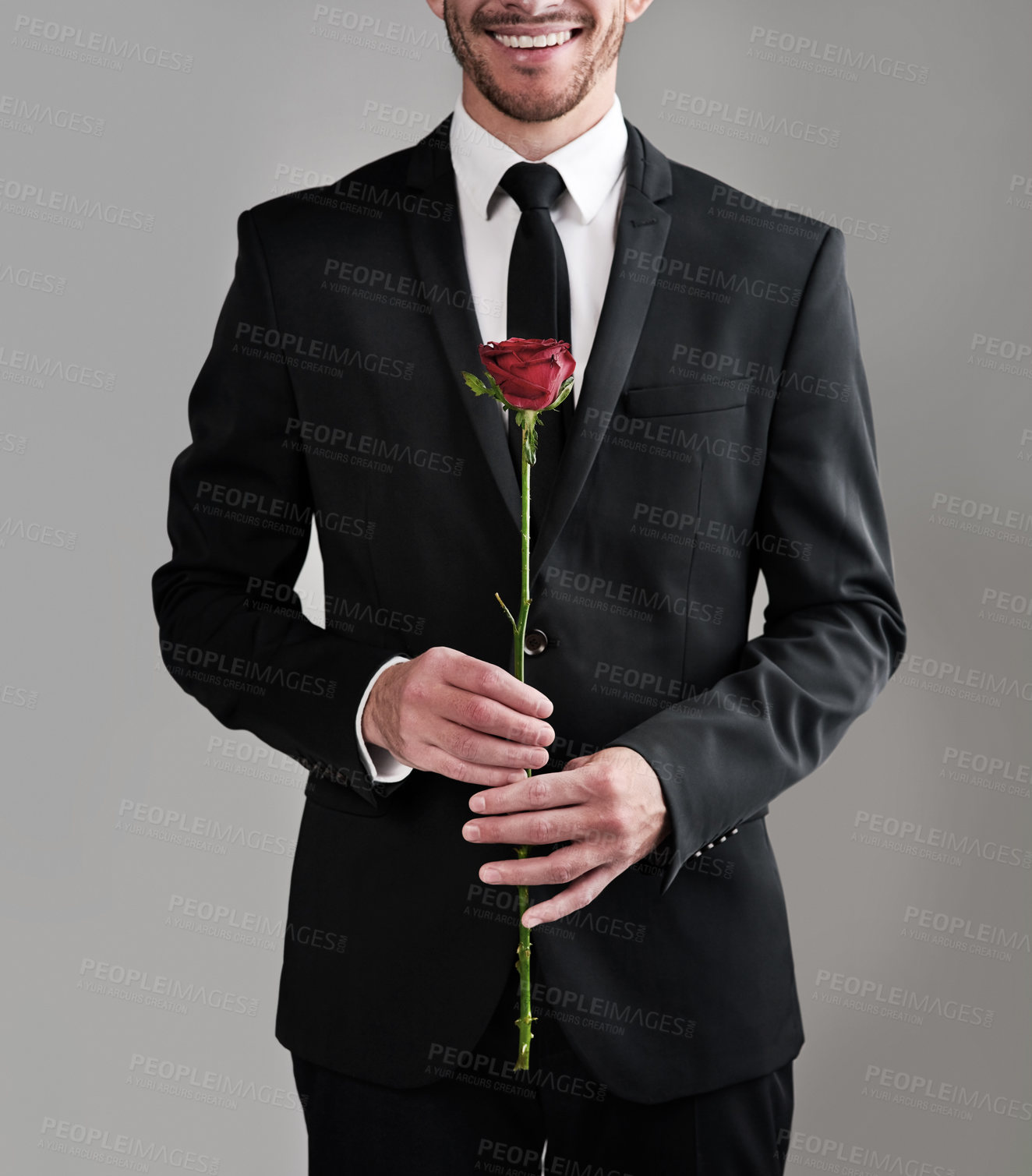 Buy stock photo Suit, hands and happy man with red rose for love, gift or celebrate valentines day. Flower, fashion and model with present for date, romance or engagement proposal isolated on gray studio background