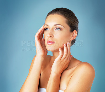 Buy stock photo Studio shot of a beautiful young woman feeling her skin against a blue background