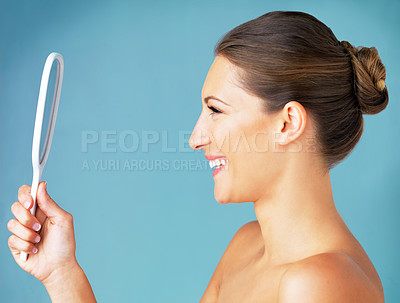 Buy stock photo Studio shot of a beautiful young woman looking at herself in the mirror against a blue background