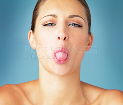 Buy stock photo Studio portrait of a beautiful young woman sticking her tongue out against a blue background