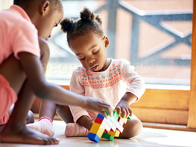 Buy stock photo a young brother and sister playing with building blocks at home. Cute little African kids playing with colorful plastic toys or blocks while sitting on the floor over the balcony background.
