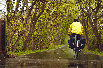 Buy stock photo Rearview shot of a male cyclist enjoying a bike ride on a wet winter's morning