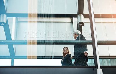 Buy stock photo Shot of a businessman and businesswoman walking and talking in a modern glass office