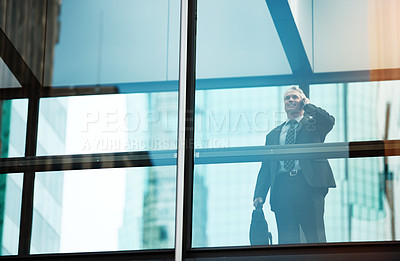 Buy stock photo Shot of a mature businessman using a mobile phone in a modern glass office