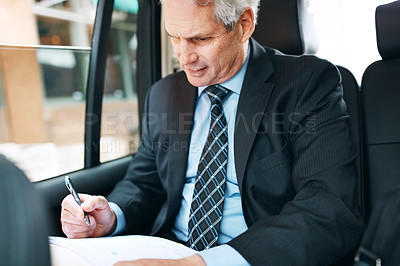 Buy stock photo Shot of a mature businessman going through paperwork in the back seat of a car