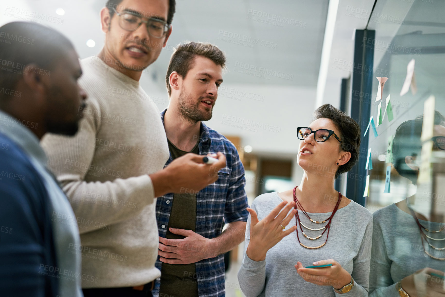 Buy stock photo Shot of a group of designers brainstorming with notes on a glass wall in an office