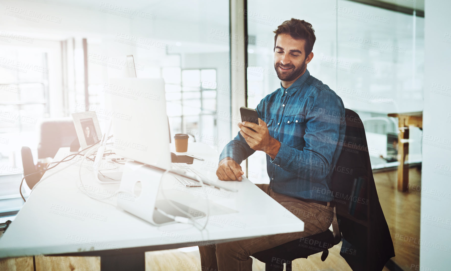 Buy stock photo Cropped shot of a handsome young businessman checking his cellphone while sitting in the office