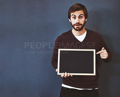 Buy stock photo Studio portrait of a young man pointing to a blackboard against a grey background
