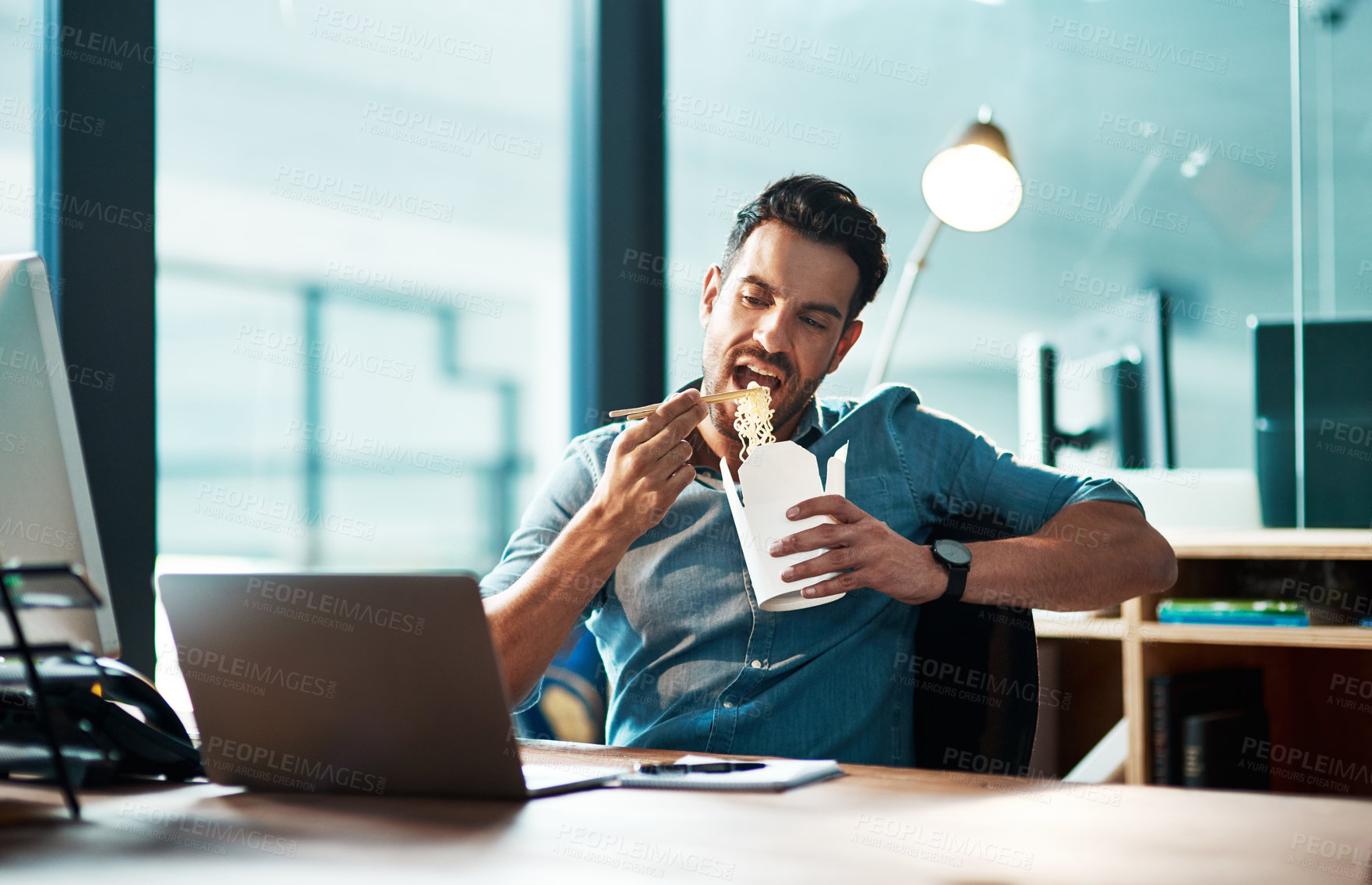 Buy stock photo Business, man and eating noodles in office at desk, laptop and working in startup company at night. Hungry young male employee, fast food and late dinner at computer technology in agency at evening