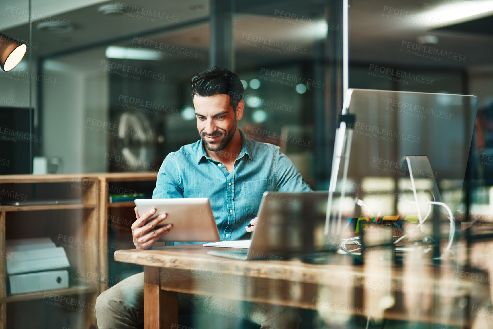 Buy stock photo Shot of a young businessman using a digital tablet at his desk in a modern office