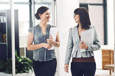 Buy stock photo Cropped shot of two young businesswomen talking while walking through their office
