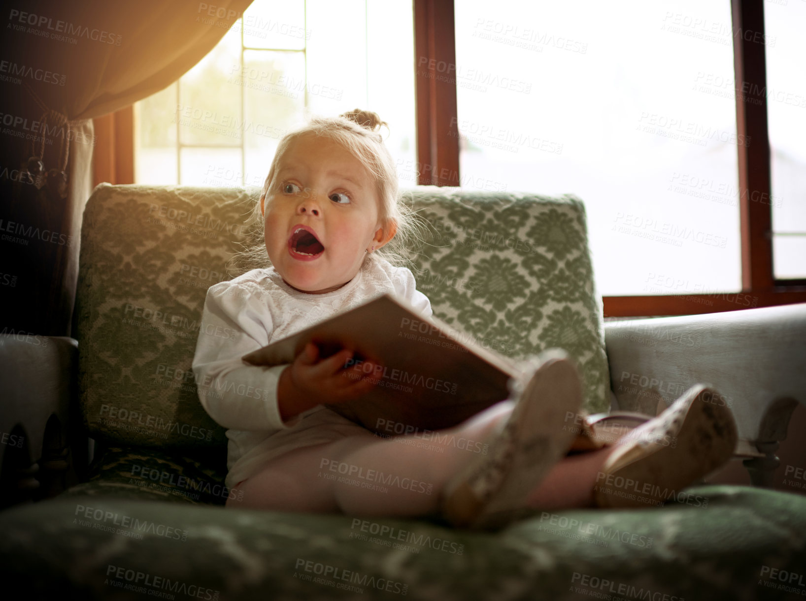 Buy stock photo Shot of an adorable little girl reading a book on the couch at home