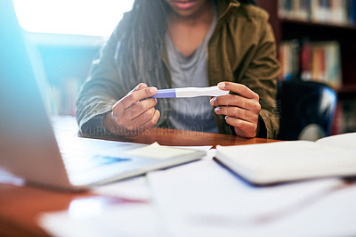 Buy stock photo Shot of an unrecognisable university student looking at the results on her pregnancy test while working in the library at campus