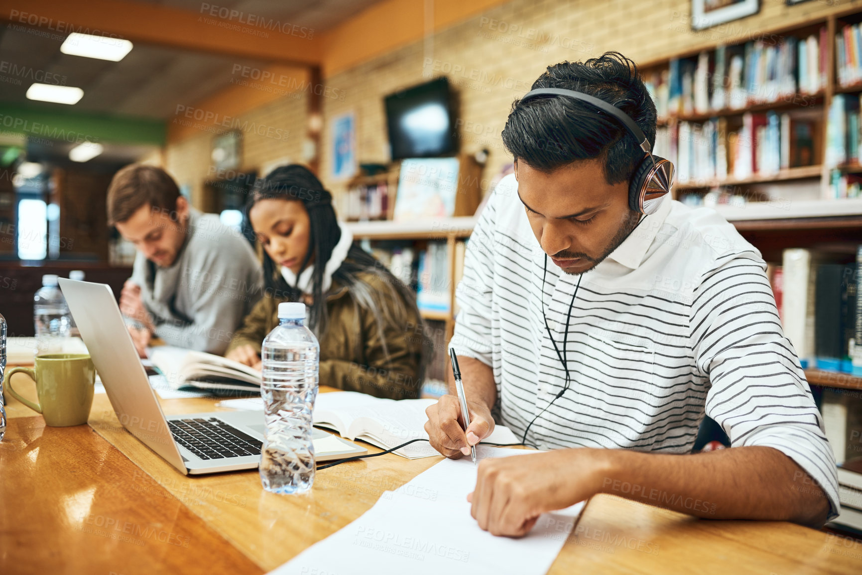 Buy stock photo Cropped shot of a young male university student studying in the library with other students in the background