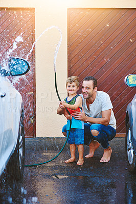 Buy stock photo Driveway, dad and child with water hose for outdoor activity or fun in summer on weekend, helping and learning. Father, boy and spraying liquid or h2o on vehicle for washing or cleaning and splash.