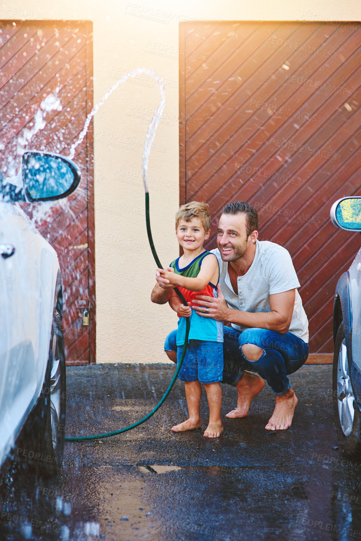 Buy stock photo Driveway, dad and child with water hose for outdoor activity or fun in summer on weekend, helping and learning. Father, boy and spraying liquid or h2o on vehicle for washing or cleaning and splash.