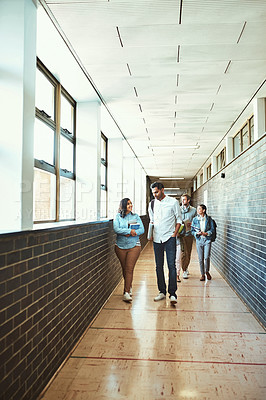 Buy stock photo Full length shot of a group of university students walking through a campus corridor