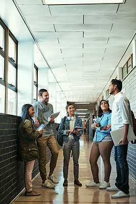 Buy stock photo Full length shot of a group of university students talking while standing in a campus corridor