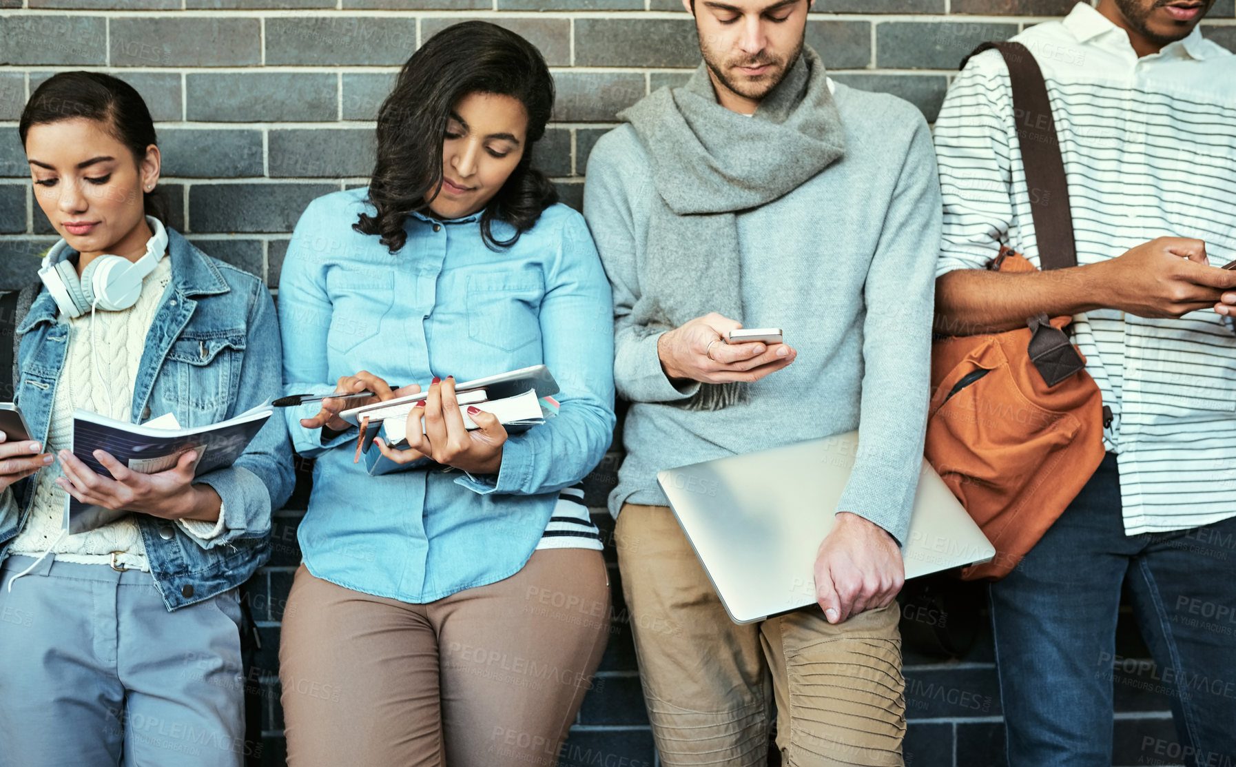 Buy stock photo Cropped shot of a group of university students using their cellphones while standing in a campus corridor