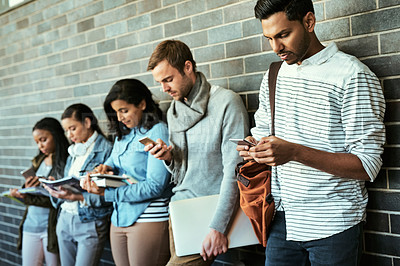 Buy stock photo Cropped shot of a group of university students using their cellphones while standing in a campus corridor