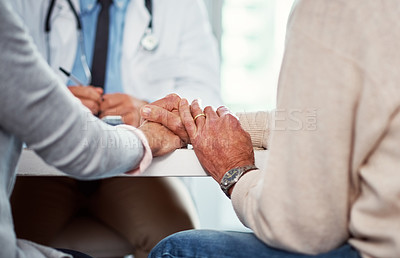 Buy stock photo Closeup shot of a senior couple holding hands in comfort while consulting a doctor in a clinic