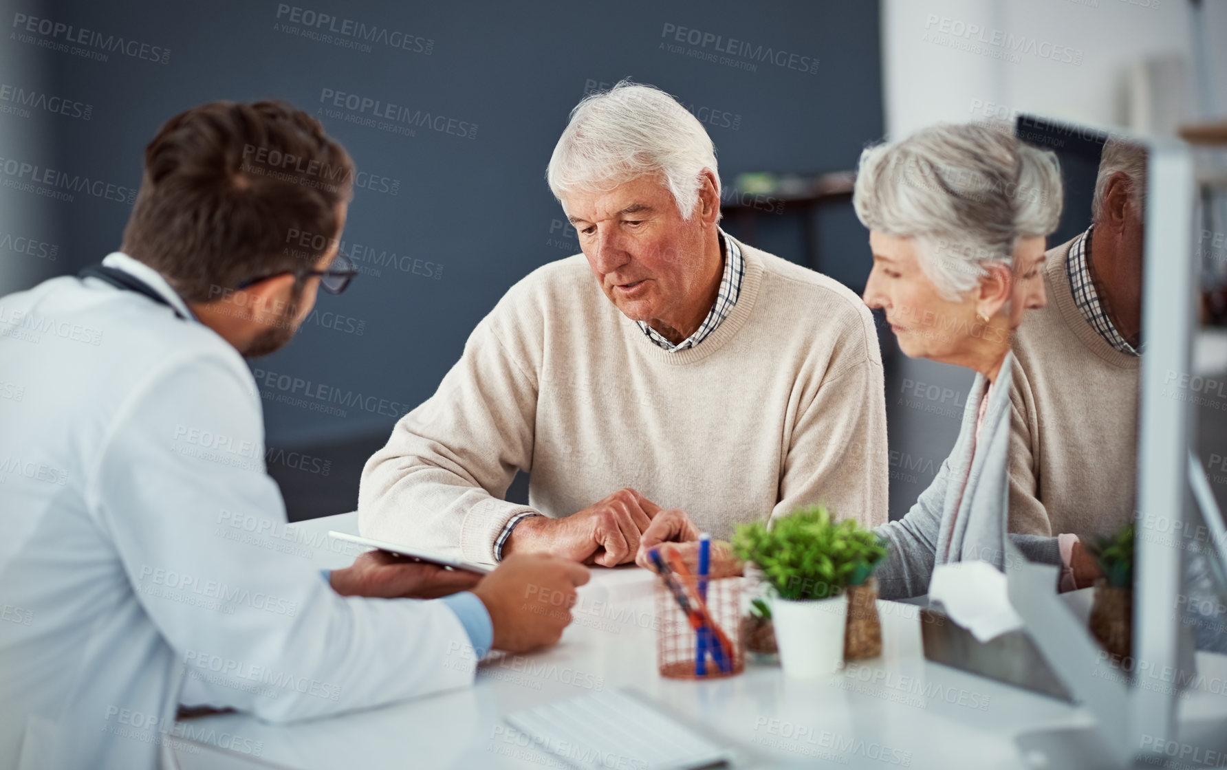 Buy stock photo Shot of a doctor discussing something on a digital tablet with a senior couple in a clinic