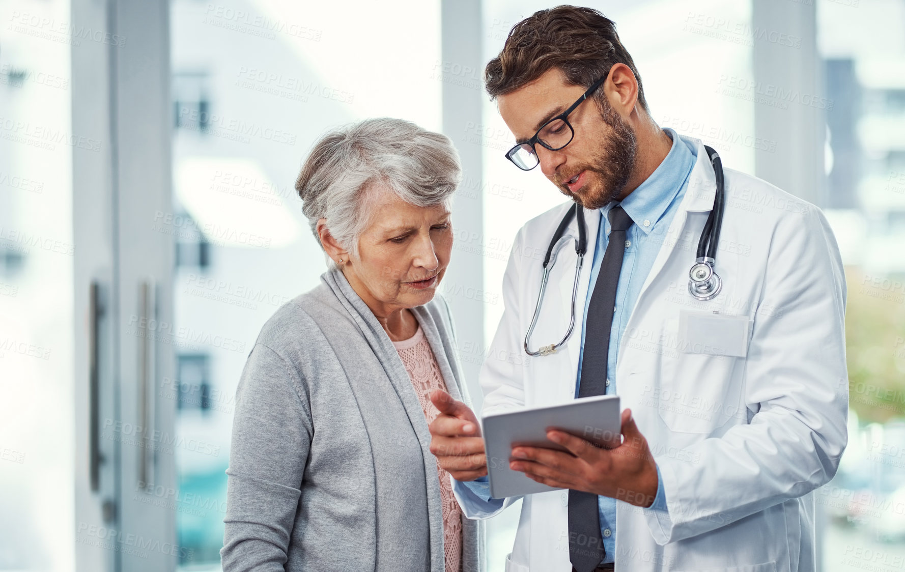 Buy stock photo Shot of a doctor discussing something on a digital tablet with a senior patient in a clinic