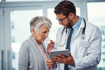 Buy stock photo Shot of a doctor discussing something on a digital tablet with a senior patient in a clinic